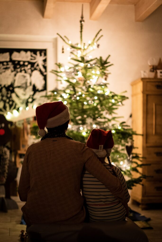 An adult hugs a young child sitting by a Christmas tree.