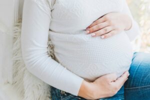 a woman wearing a white shirt cradles her baby bump and contemplates how to reduce toxin exposure to her unborn child.